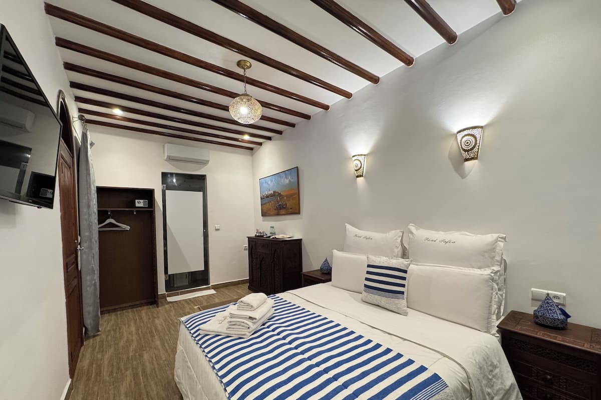 A bedroom with a bed, a dresser, a nightstand, a painting, and a ceiling fan.