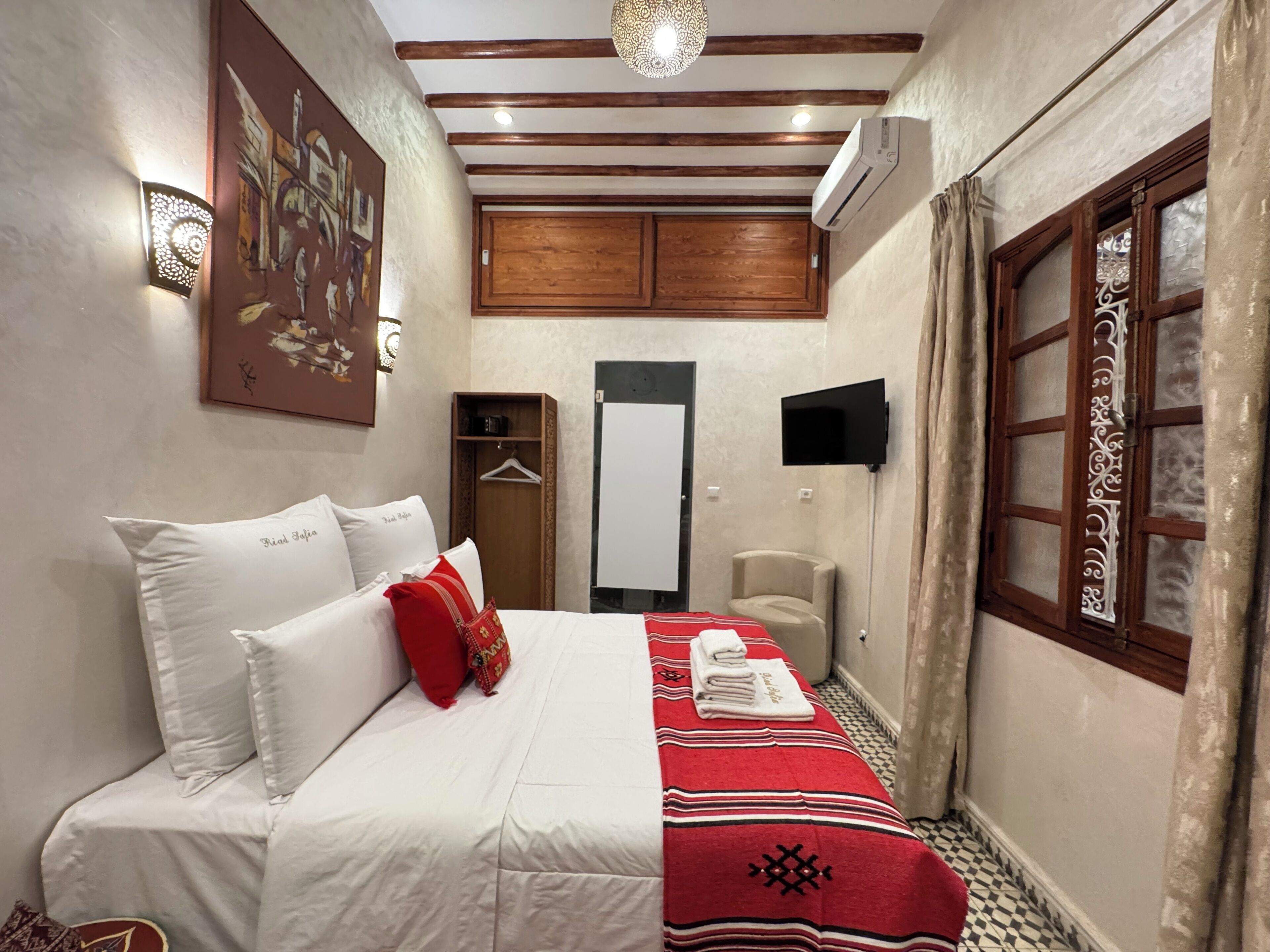 A hotel room with a bed, a wardrobe, a television, and a window with curtains.