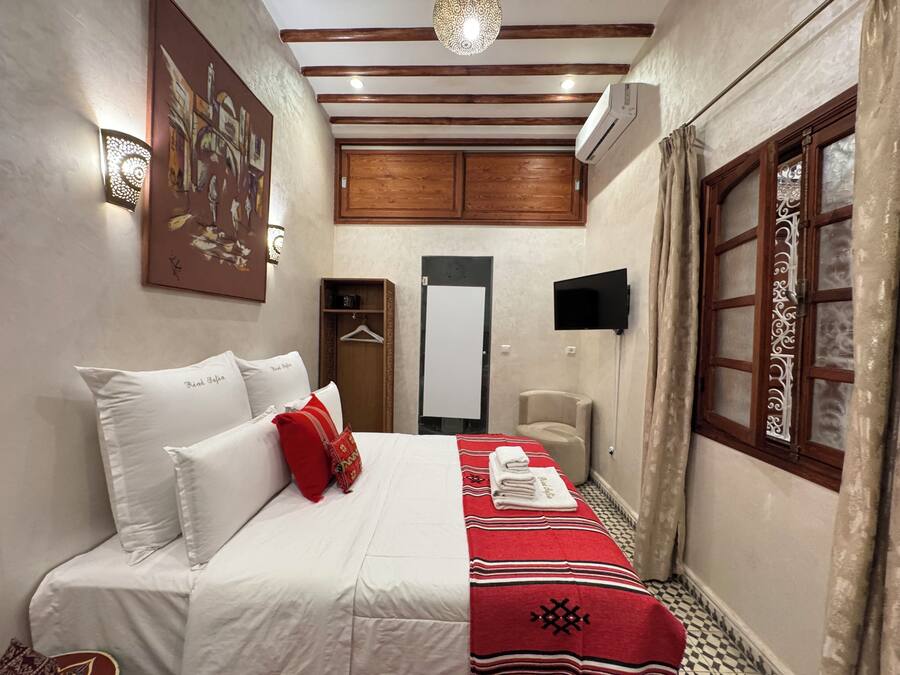 A hotel room with a bed, a wardrobe, a television, and a window with curtains.