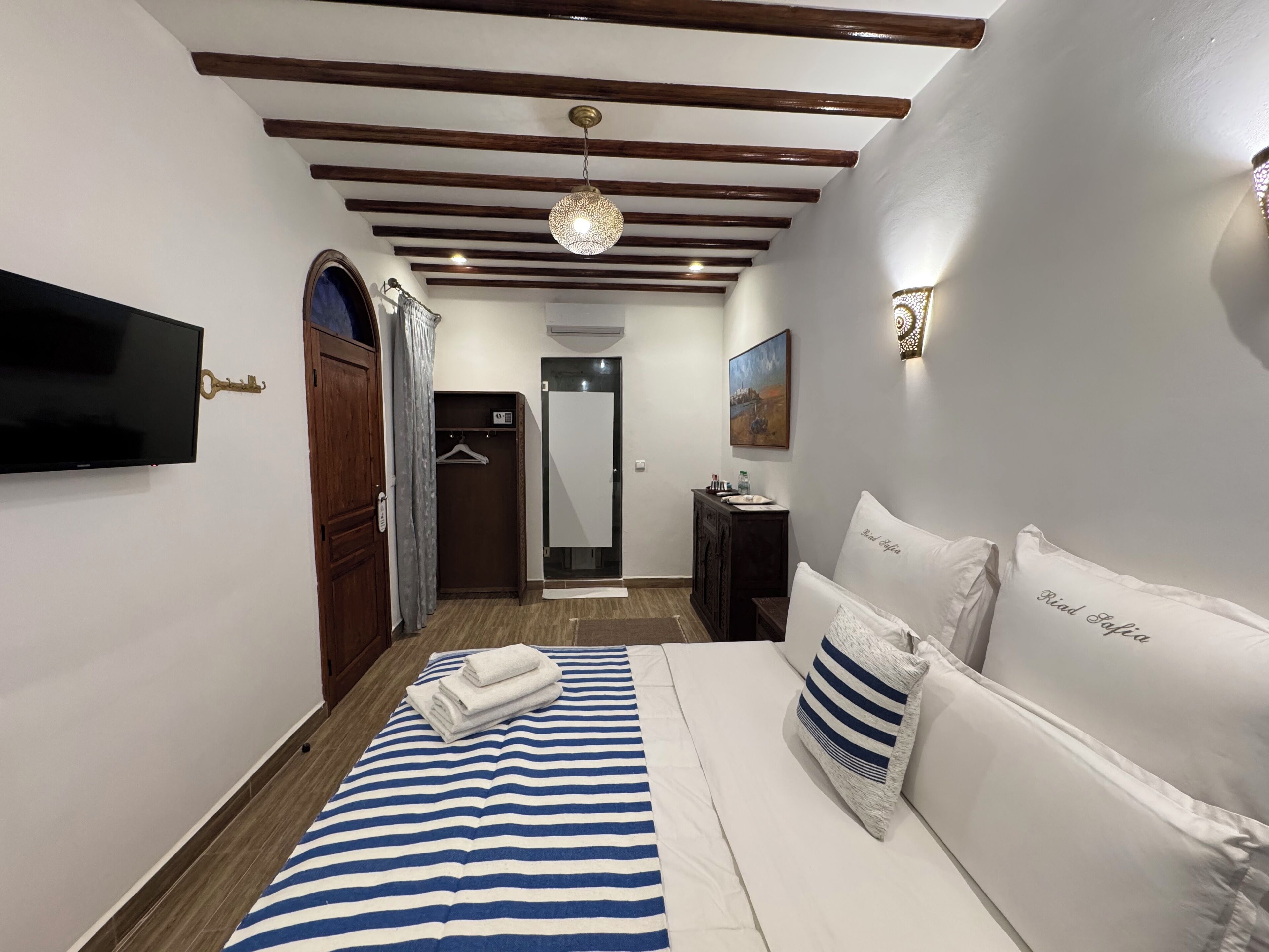 Un dormitorio con cama, televisión, armario, espejo y un cuadro en la pared.