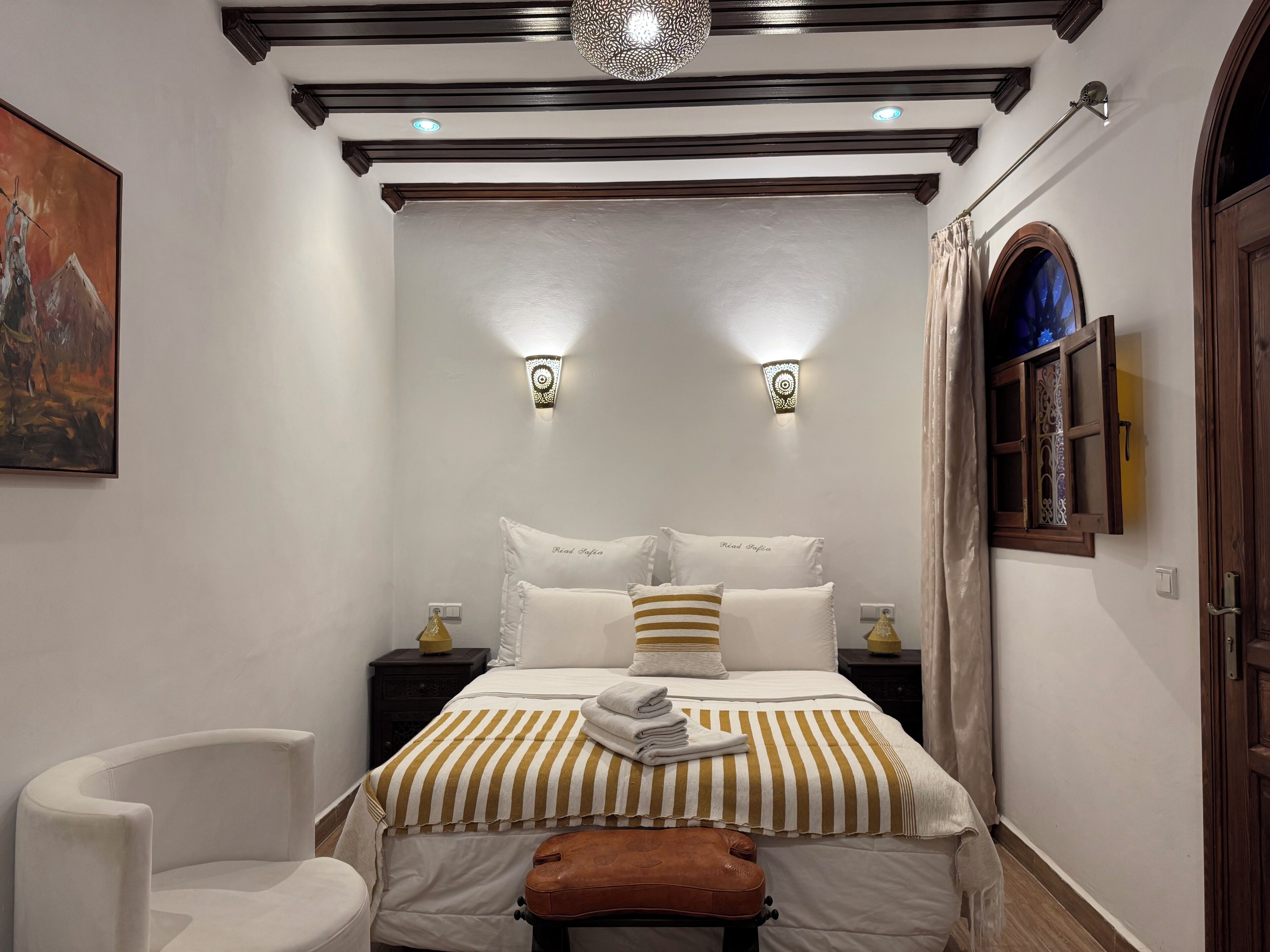 Una camera da letto con un letto, due comodini, una sedia, una panca e un quadro appeso al muro.