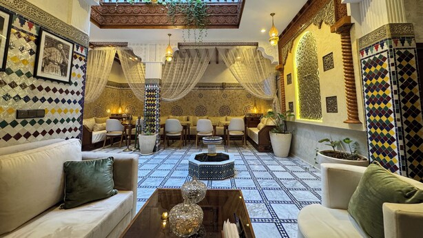 A traditional interior with patterned walls, a balcony with a railing, and a seating area with sofas and tables. - Riad Safia (Rabat)