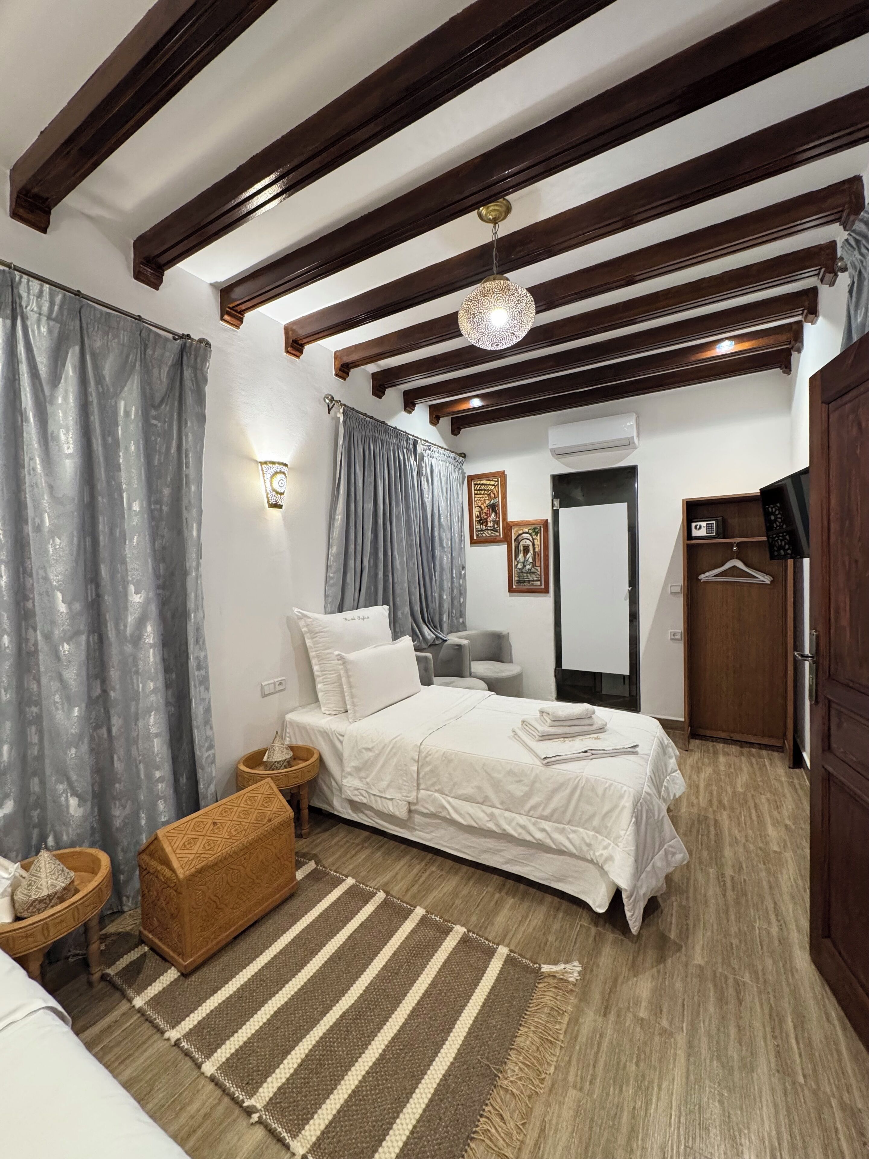 Un dormitorio con cama, cabecera de madera, lámpara colgante, espejo y armario.