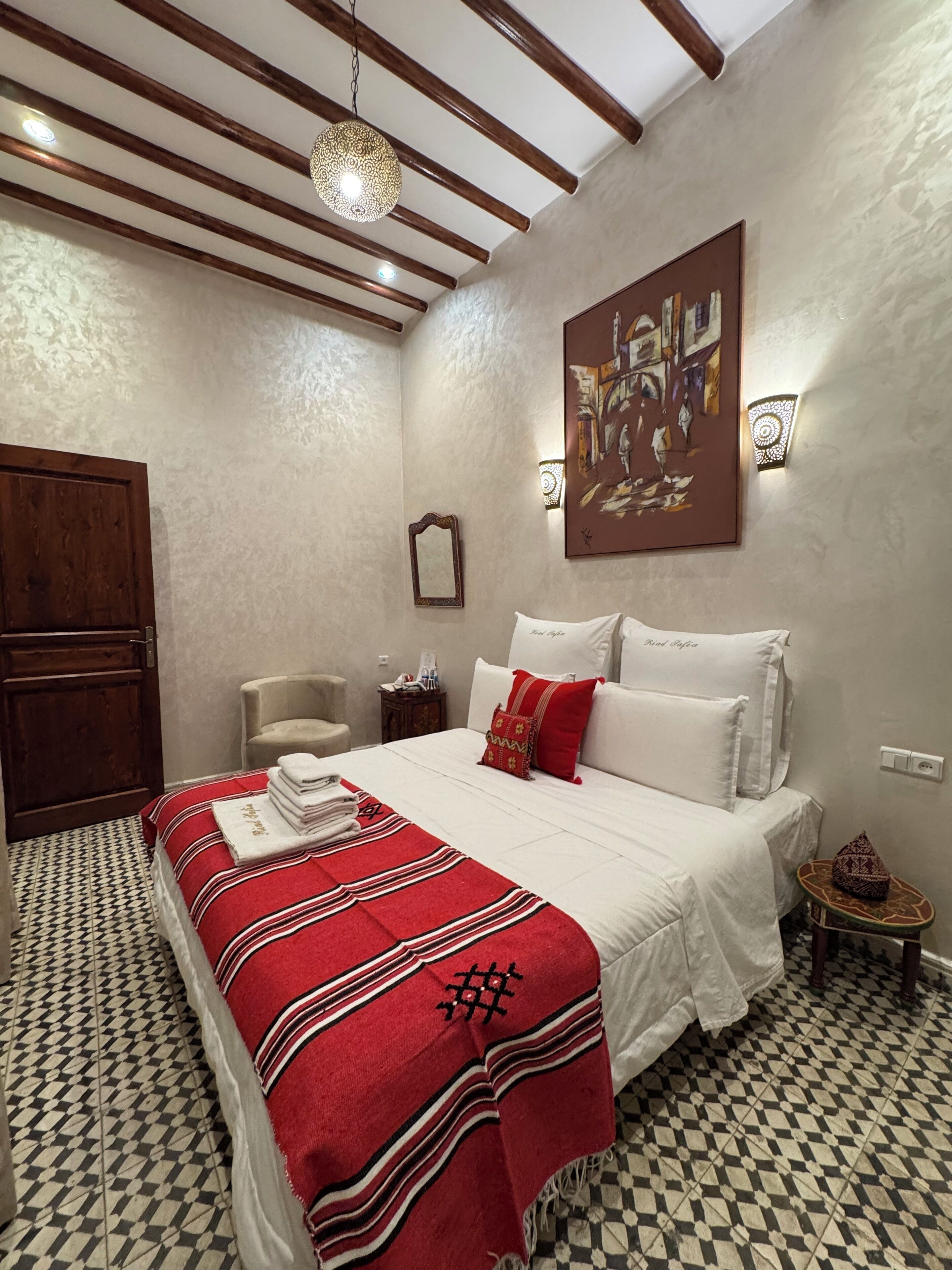 A hotel room with a bed, a chair, a nightstand, and a small table.