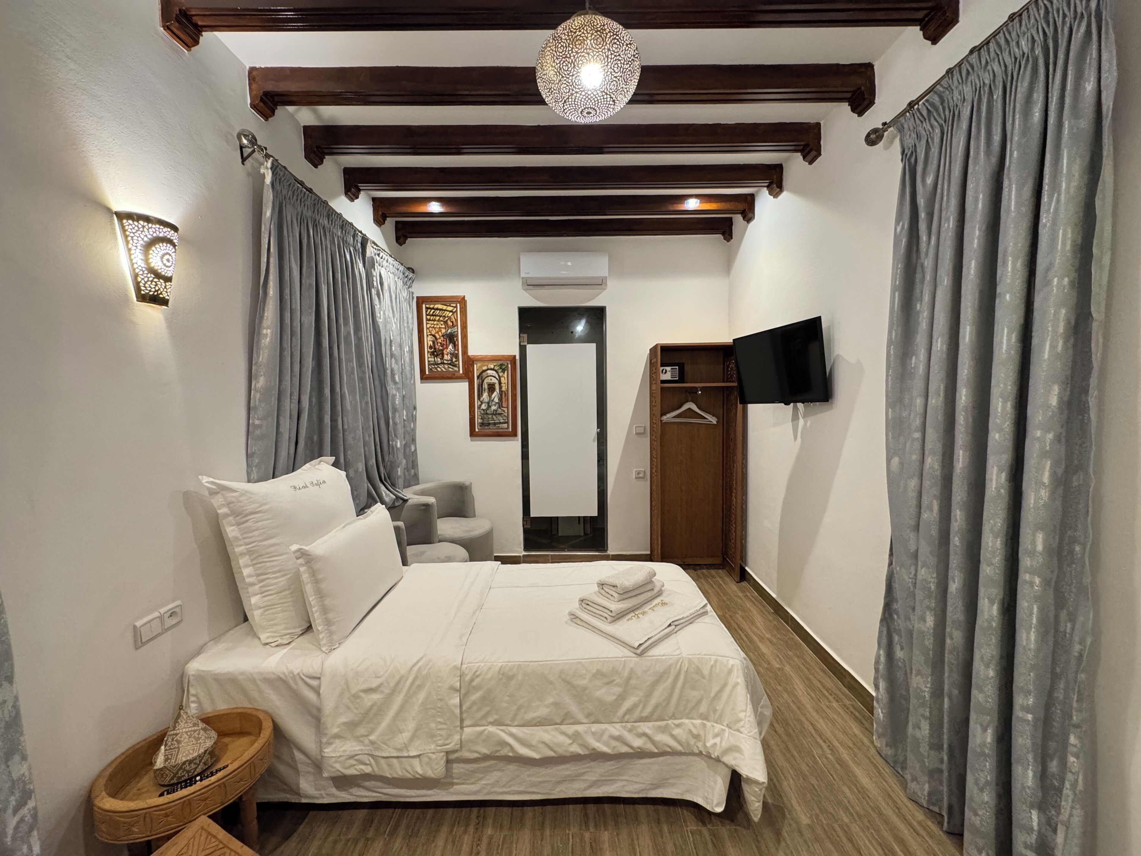 Un dormitorio con cama, mesita de noche y televisor montado en la pared.
