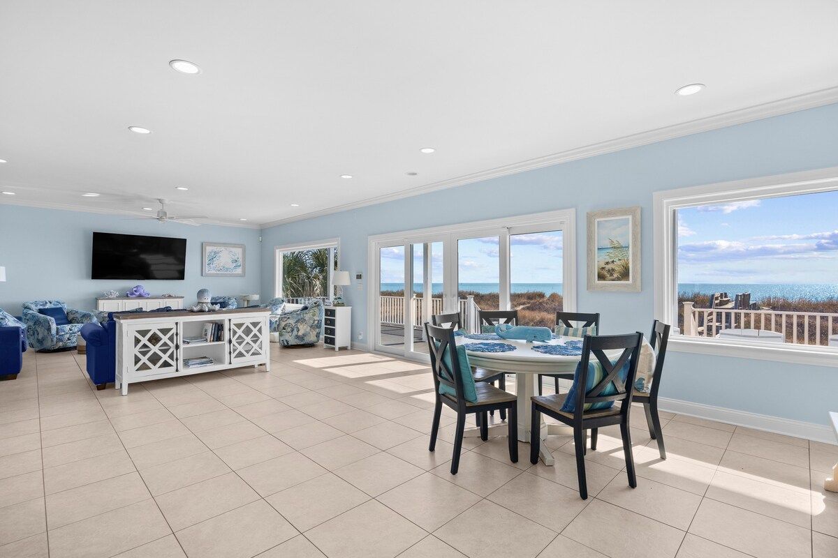 A spacious living room with a dining area, large windows, and a view of the ocean.