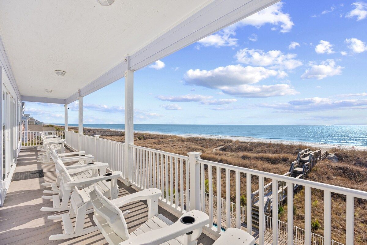 Eine überdachte Terrasse mit weißen Stühlen und Blick auf den Strand.