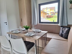Un comedor con una mesa dispuesta para dos, una ventana que ofrece vistas a un edificio y un sofá con un cojín.