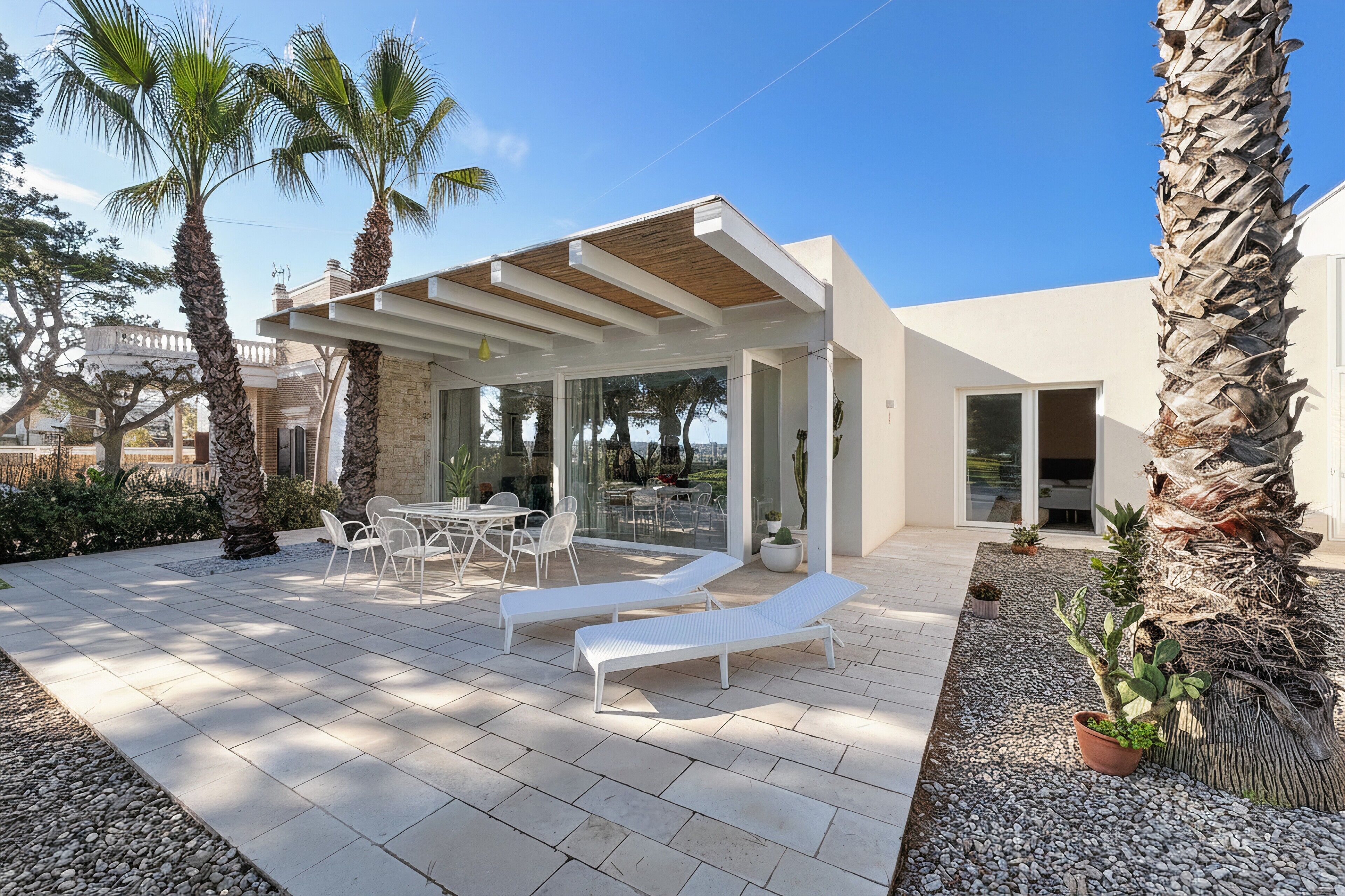 A modern outdoor patio with lounge chairs, a table, and a pergola.