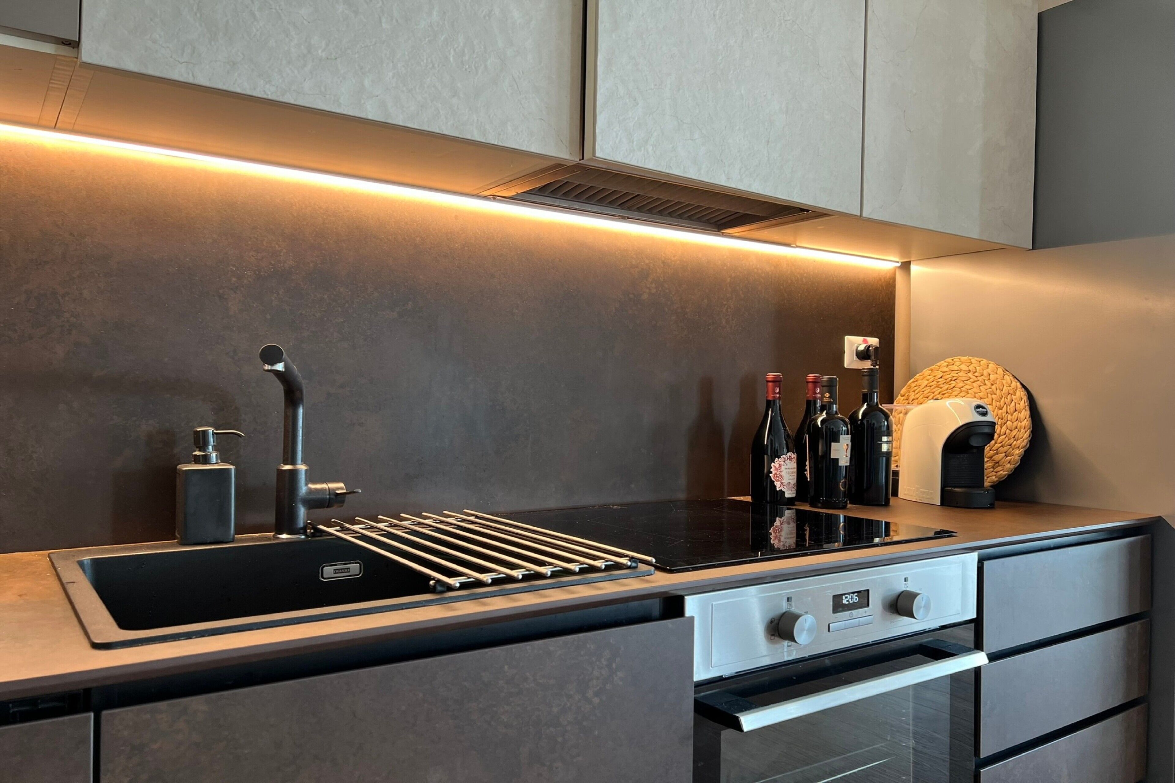 Une cuisine moderne dotée d’un four encastré, d’un évier en acier inoxydable et d’un plan de travail muni d’un porte-bouteilles à vin.