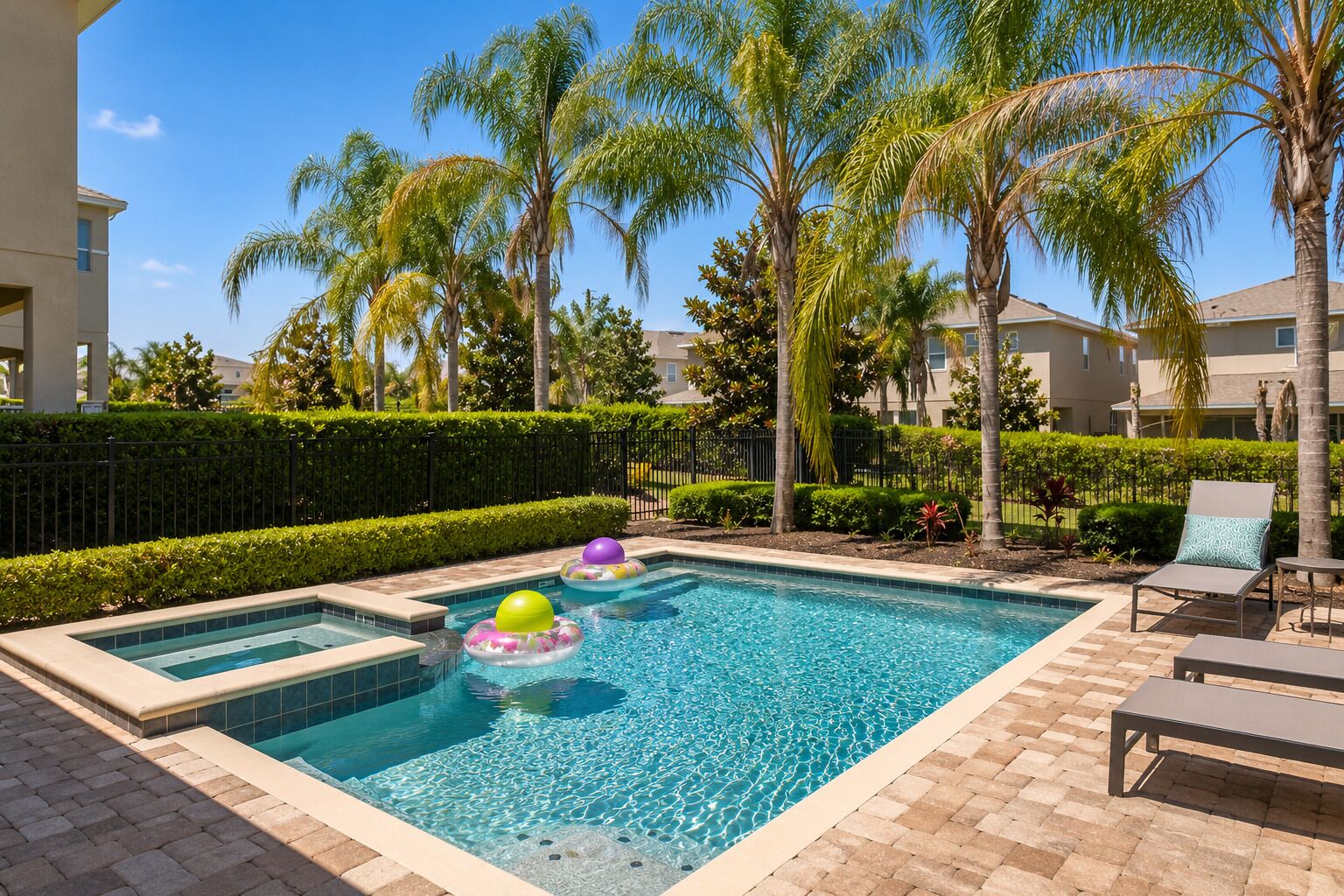 Una piscina rectangular con borde de azulejos, rodeada por un patio de ladrillo. Hay sillas de descanso y una mesita en el patio.