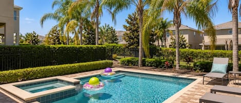 Una piscina rectangular con borde de azulejos, rodeada por un patio de ladrillo. Hay sillas de descanso y una mesita en el patio.
