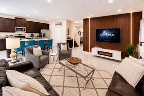 A modern living room with a flat-screen TV, comfortable seating, a kitchen in the background, and a 'TOGETHER' sign on the wall. - Casa Encore Resort/Piscina privativa/5 Quartos (Kissimmee)