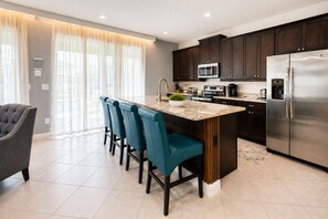 Een moderne keuken met donkere kastjes, roestvrijstalen apparatuur en een bar met teal-kleuren stoelen.