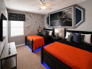 Een slaapkamer met twee bedden, een plafondventilator, een muur met een Star Wars muurschildering en een groot, ingelijst schilderij.