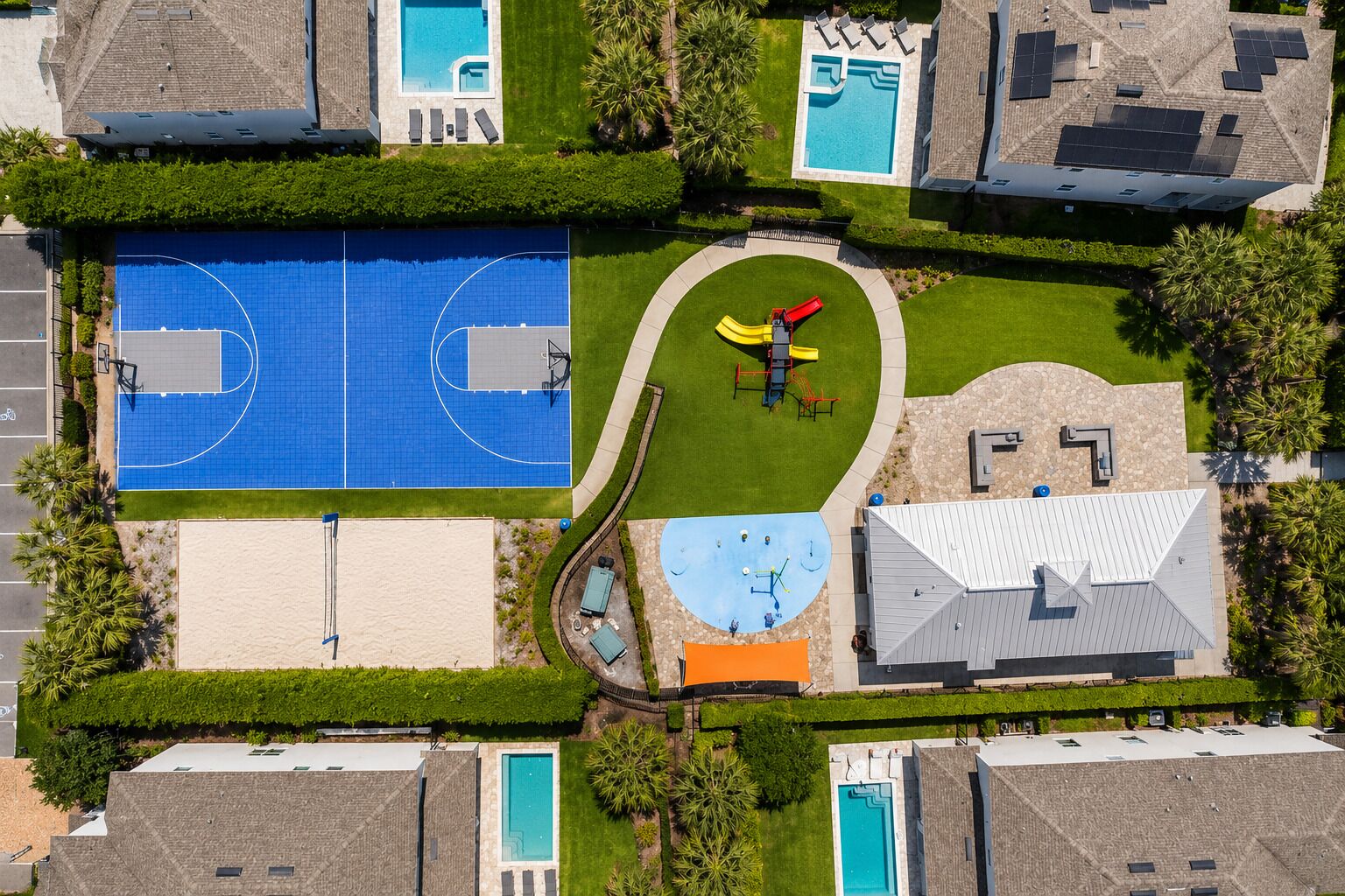 Vue aérienne d’un quartier résidentiel avec une piscine, des terrains de basketball et une aire de jeux.