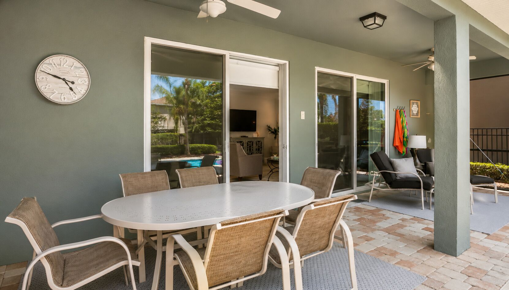 A covered patio with a round table and chairs, a ceiling fan, and a clock on the wall.