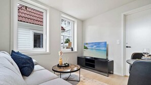 Ein Wohnzimmer mit Sofa, Couchtisch, Fernseher und einem Essbereich mit Stuhl und einem Glas Wein.