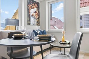 Un coin repas avec une table ronde dressée pour deux personnes, deux assiettes, deux verres à vin et un petit vase avec des fleurs.