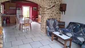 Ein Wohnzimmer mit steinernen Bogen, ein Essbereich mit Stühlen und Tisch, eine Couch und eine Küche mit Schränken und einer Mikrowelle.