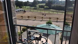 Ein Balkon mit Blick auf eine Freiluftarena, eine Steinsäule und einen Sitzbereich mit Sonnenschirmen.