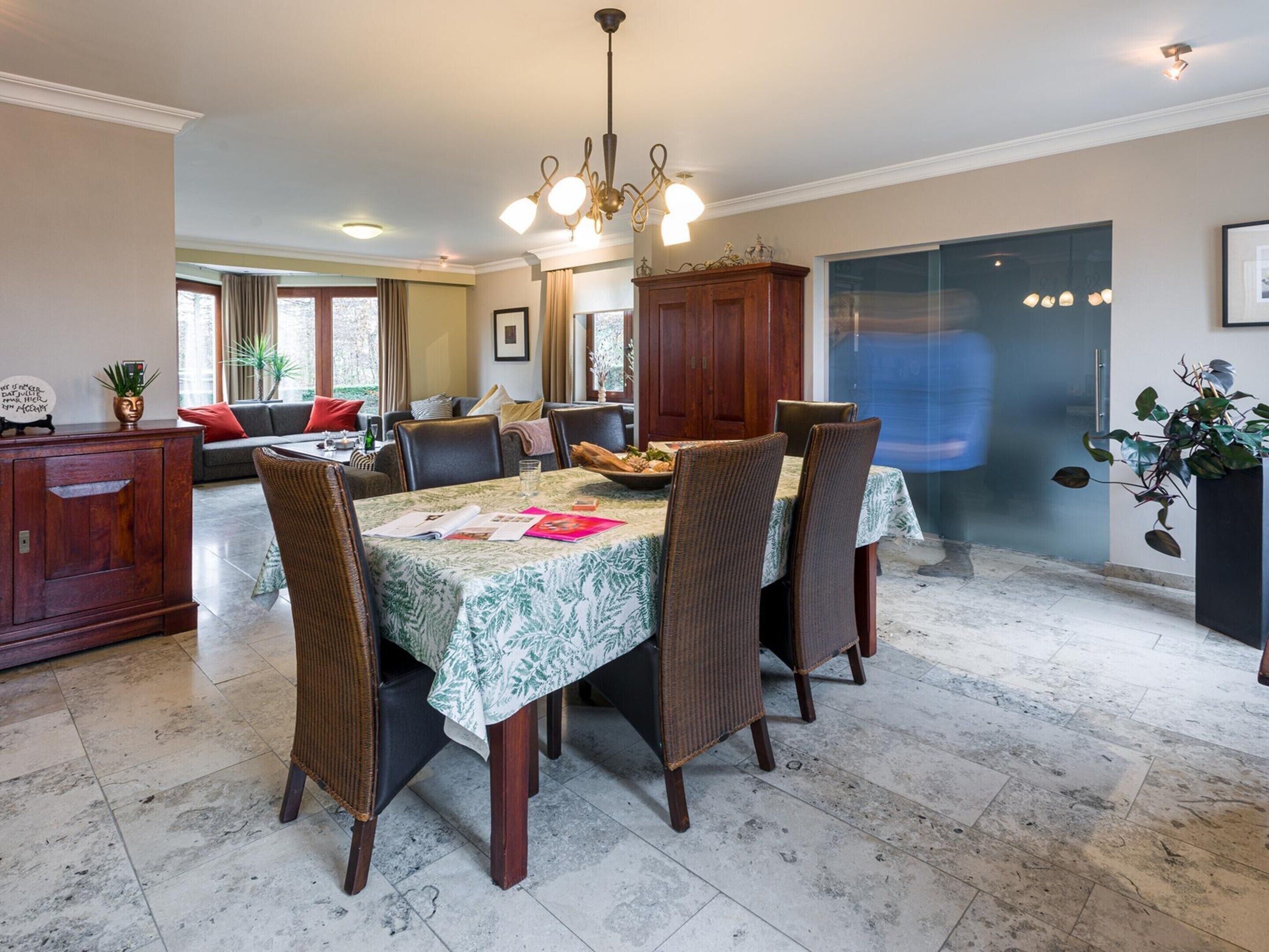 A dining area with a table set for four, surrounded by wicker chairs, a chandelier, and a cabinet with a vase.