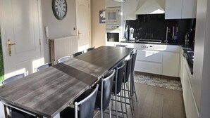 A modern kitchen with a wooden table and chairs, white cabinets, a microwave, and a coffee maker. - Group Accommodation in Borgloon Hof Van Kalenberg (Borgloon)