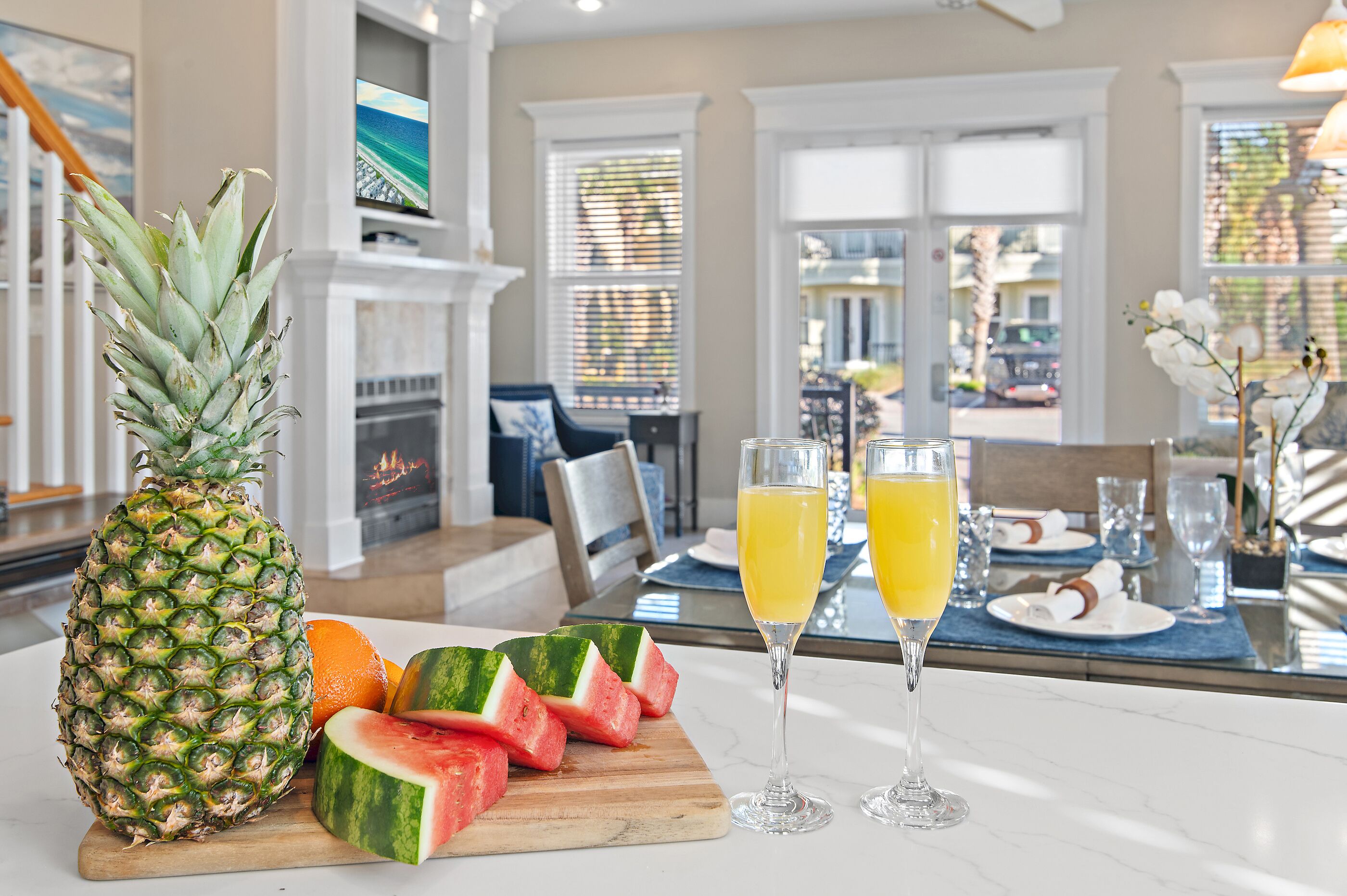 A dining area with a pineapple, watermelon slices, and two glasses of orange juice on a marble table.
