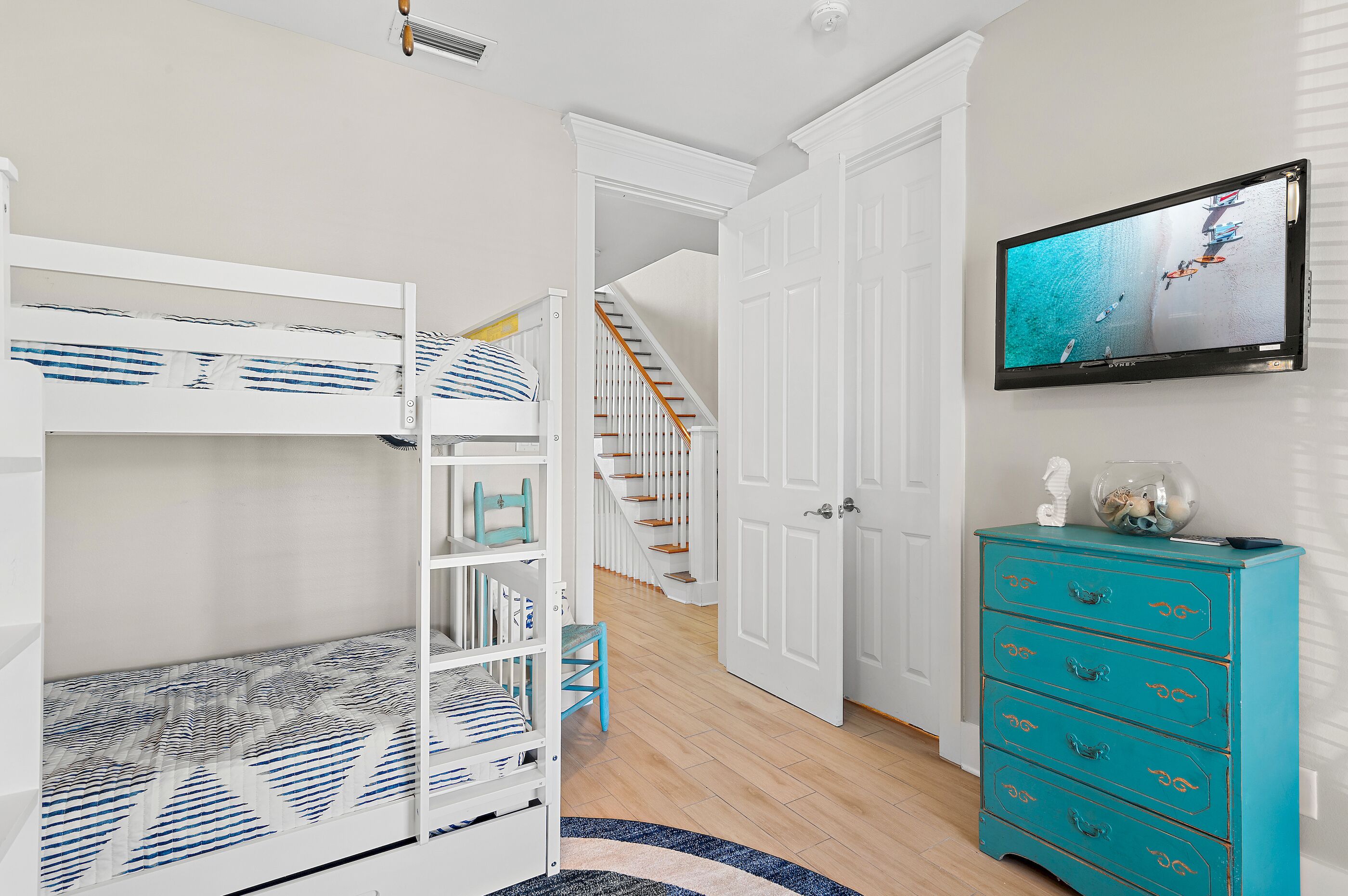 A room with a bunk bed, a teal dresser, a television, and a staircase leading to another room.