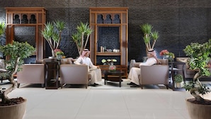 A lobby with two men seated on sofas, a decorative wall, and potted plants. - Sedra Global Hotel Jeddah (Jeddah)