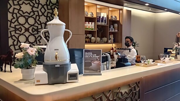 Un área de recepción de hotel moderna con mostrador, máquina de café, cartel y decoración en la pared.