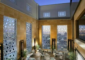 An indoor courtyard with seating, decorative screens, and a view of the city. - Sedra Global Hotel Jeddah (Jeddah)