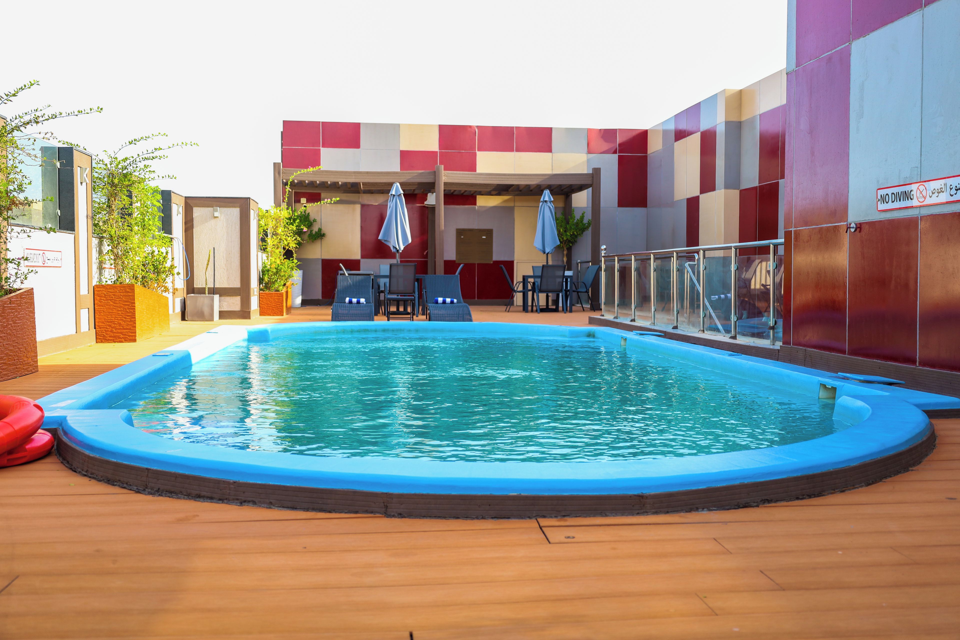 An outdoor swimming pool with lounge chairs and umbrellas, surrounded by a building with a red and beige color scheme.