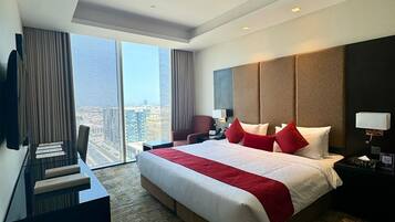 Habitación de hotel con una cama grande, un escritorio, una silla, un televisor y vistas a la ciudad.