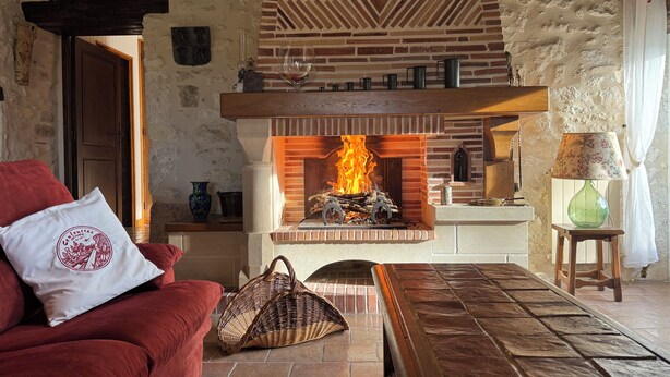 Un salon chaleureux avec une cheminée en briques, un canapé rouge et un panier en osier.