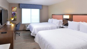 Quarto de hotel com duas camas, uma escrivaninha, uma cadeira, televisão e janela com vista.