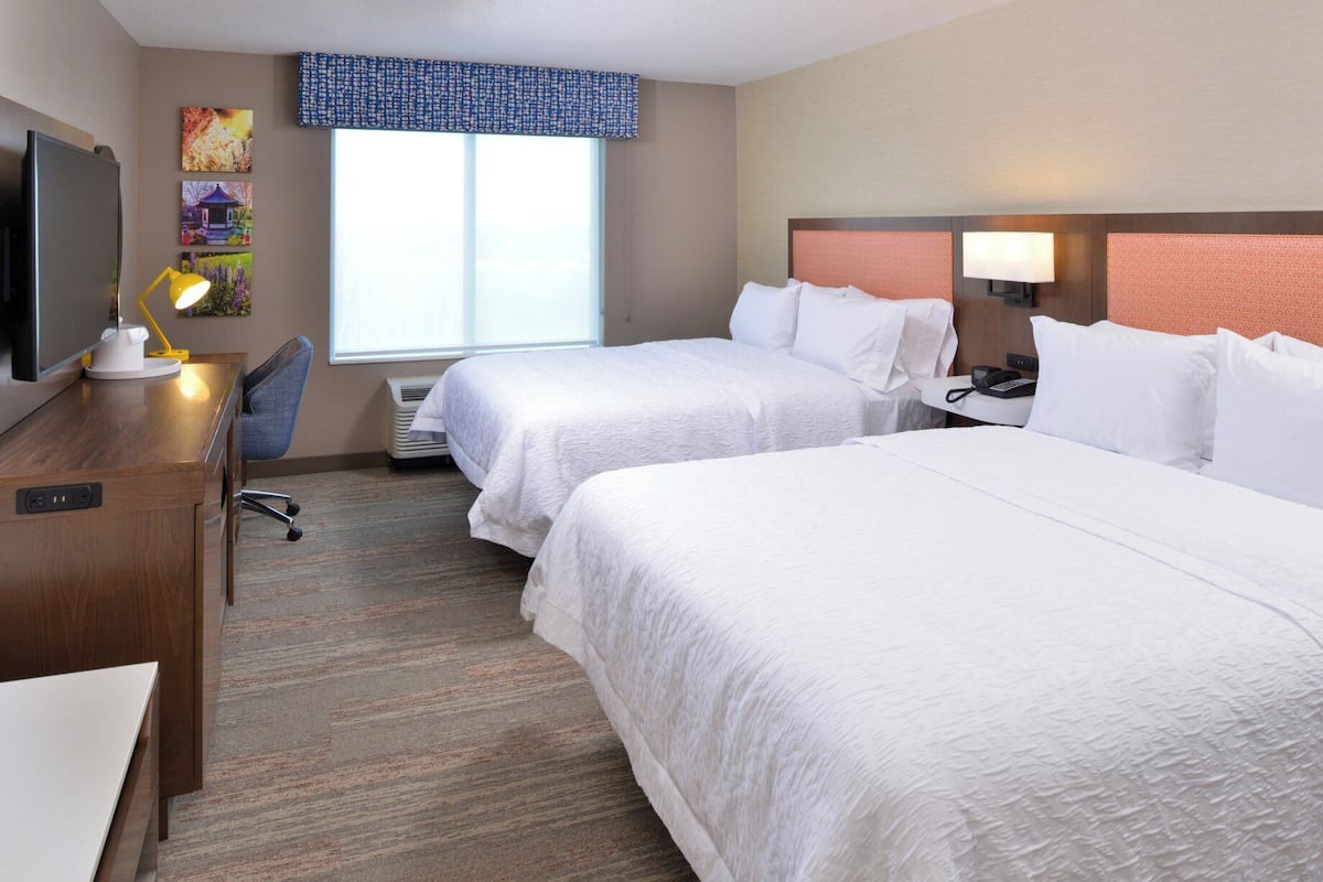 A hotel room with two beds, a desk, a chair, a TV, and a window with a view.
