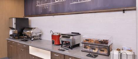 A kitchenette with a chalkboard sign reading "EAT", a grill, a coffee machine, and a display case with pastries.