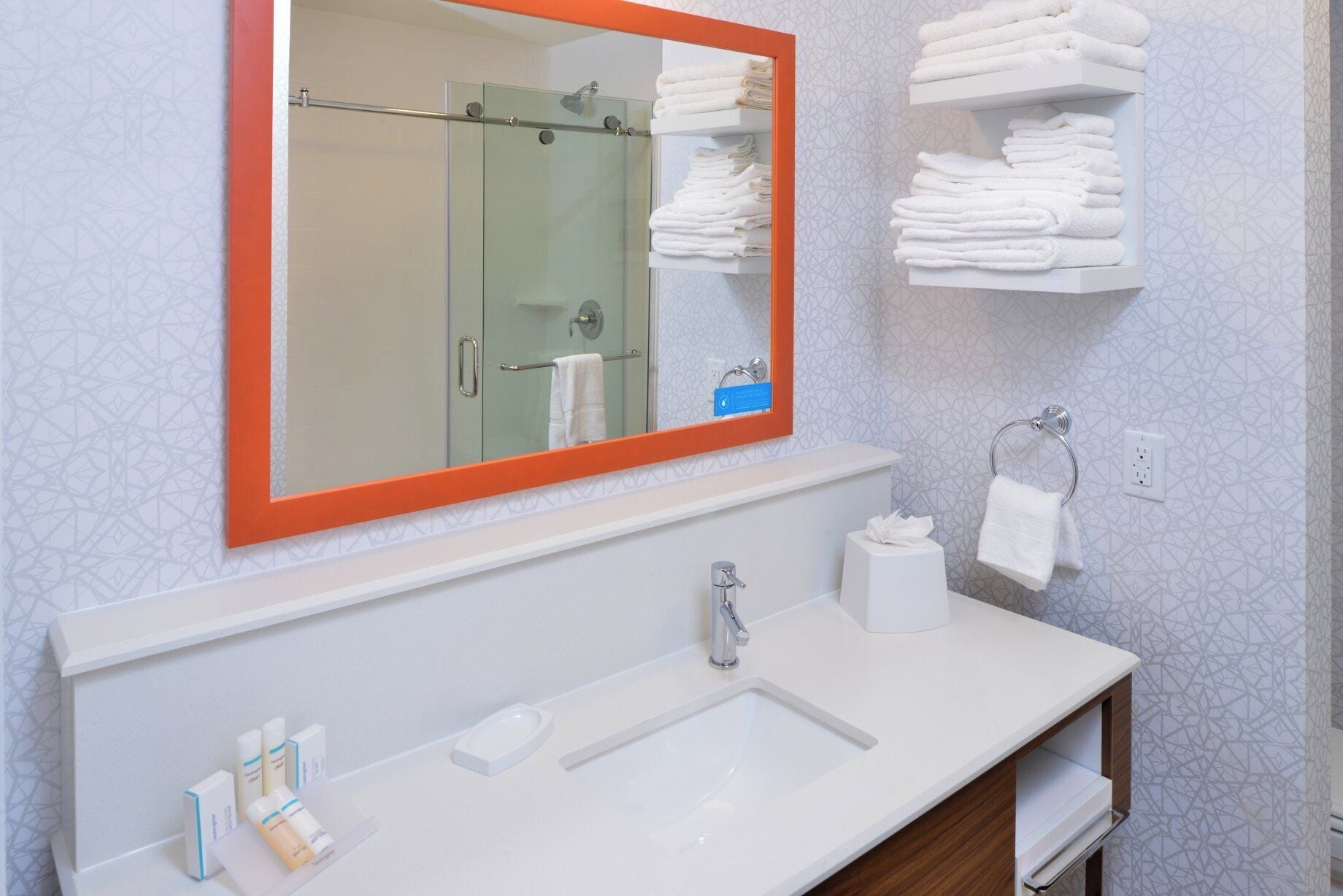 A bathroom with a glass shower enclosure, a white sink, and a mirror with an orange frame.