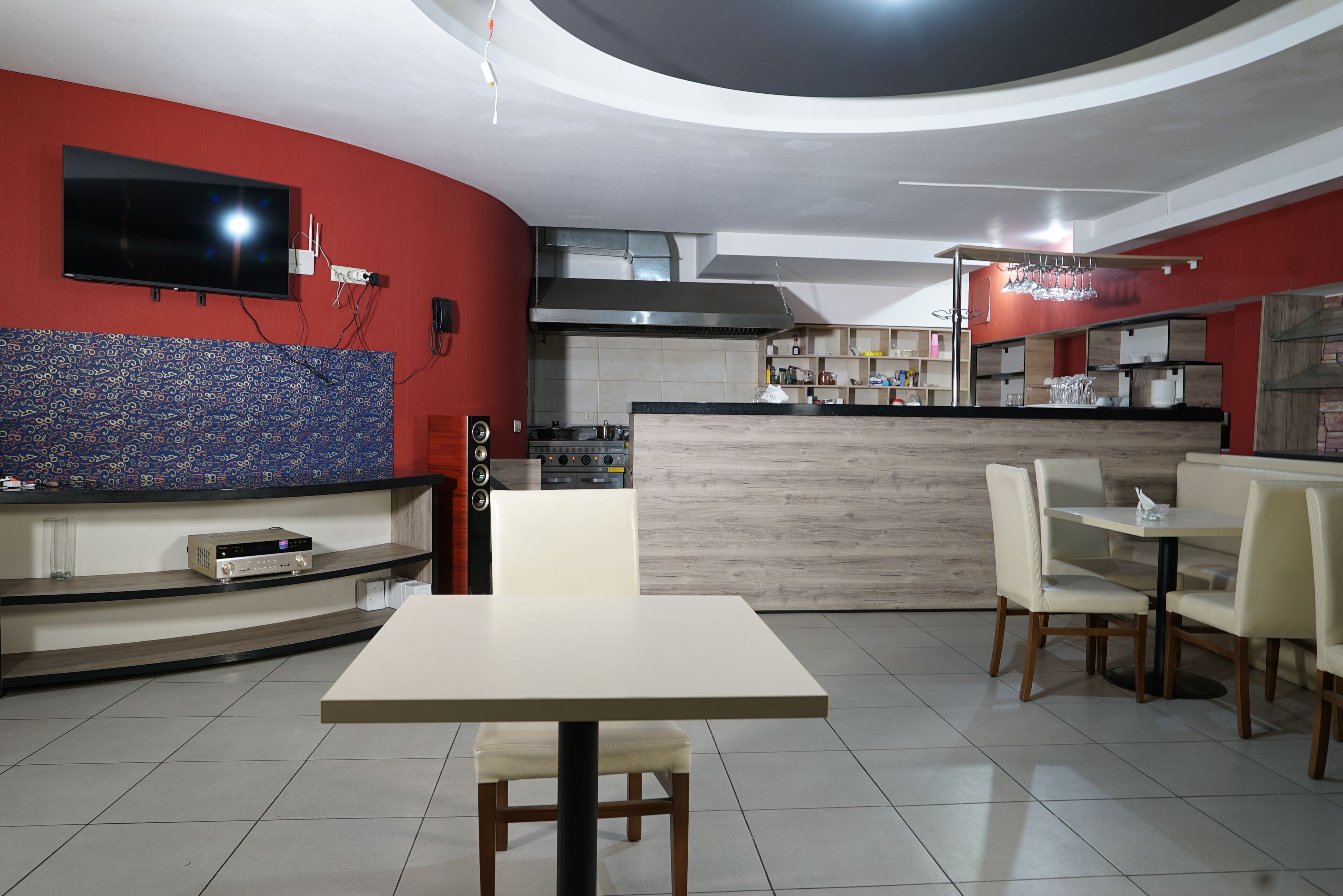 A restaurant with a TV mounted on the wall, a counter with a grill, and a seating area with tables and chairs.