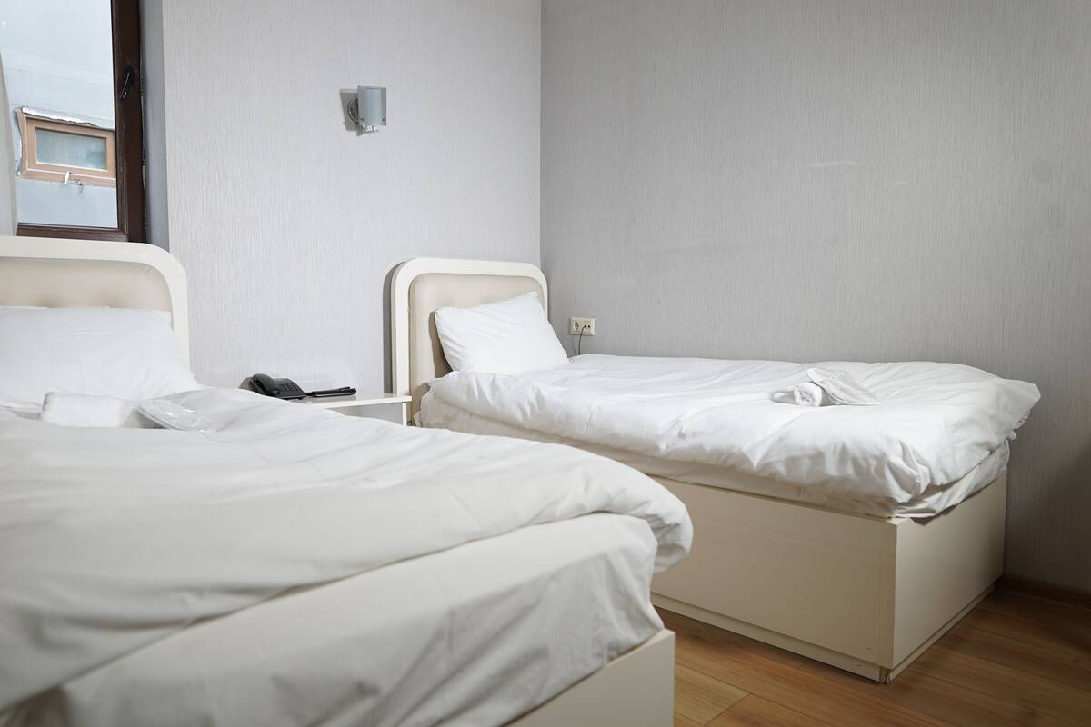 Two beds in a room with a window, a wall socket, and a small table.