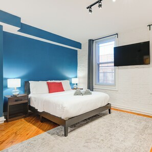 A modern bedroom with a bed, nightstands, a flat-screen TV, and a window with blinds. - 303 N 3rd St B2 (Philadelphia)