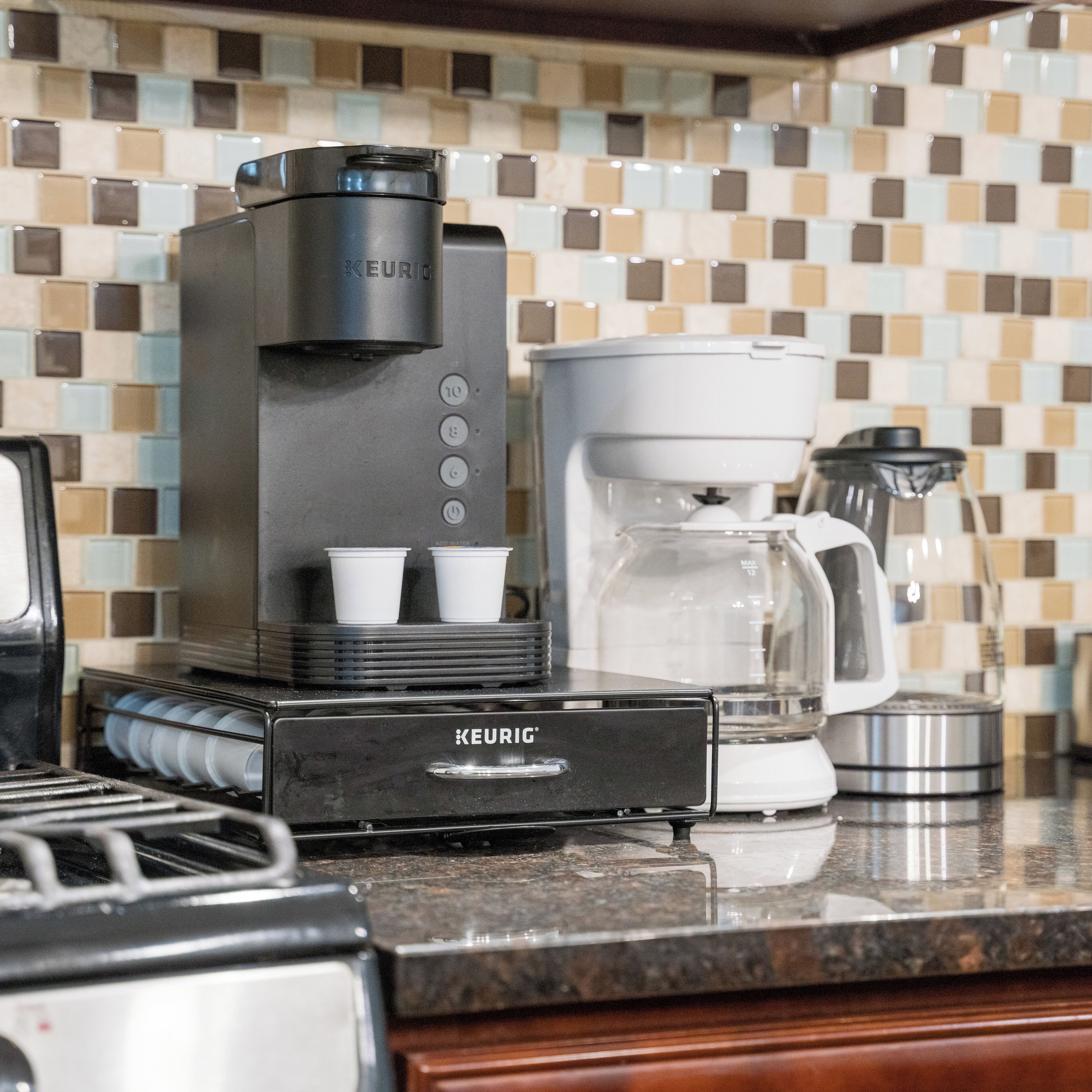 Una macchina per il caffè Keurig con raccoglitore di gocce, caraffa e serbatoio dell'acqua su un piano di lavoro in cucina.