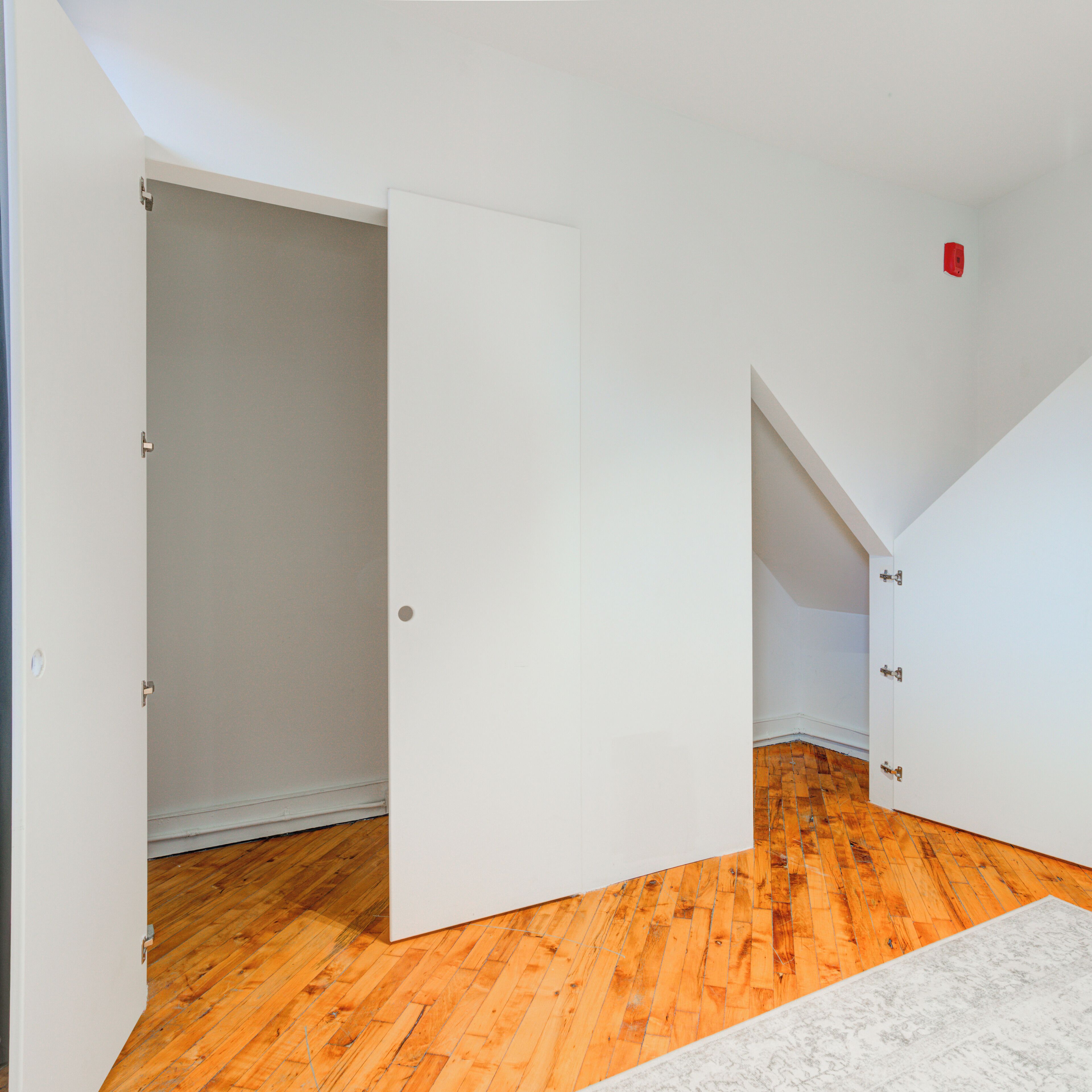 Una habitación con piso de madera, paredes blancas y una puerta blanca.