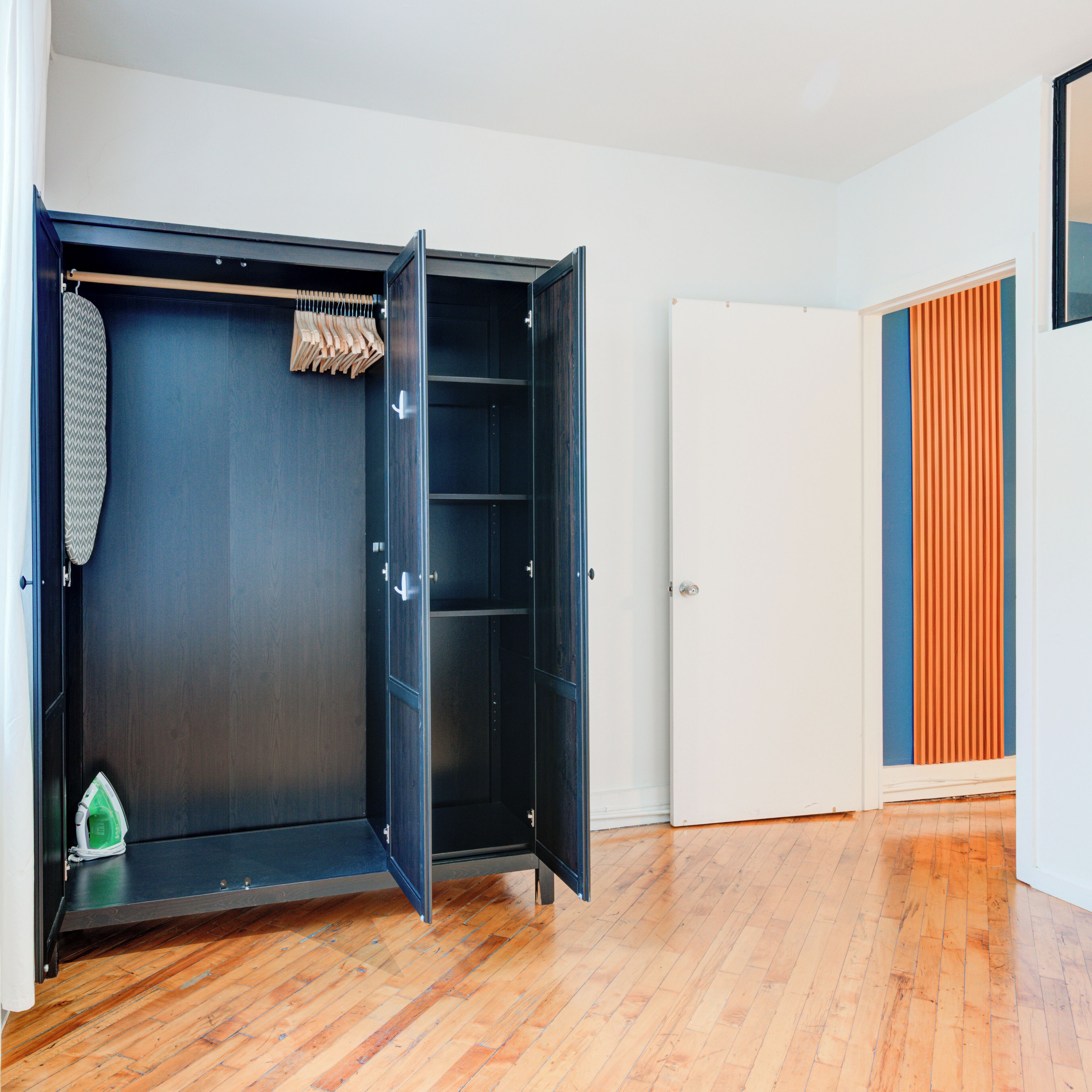 Un dressing avec des finitions en bois foncé, une tringle à vêtements et une porte avec un panneau blanc.