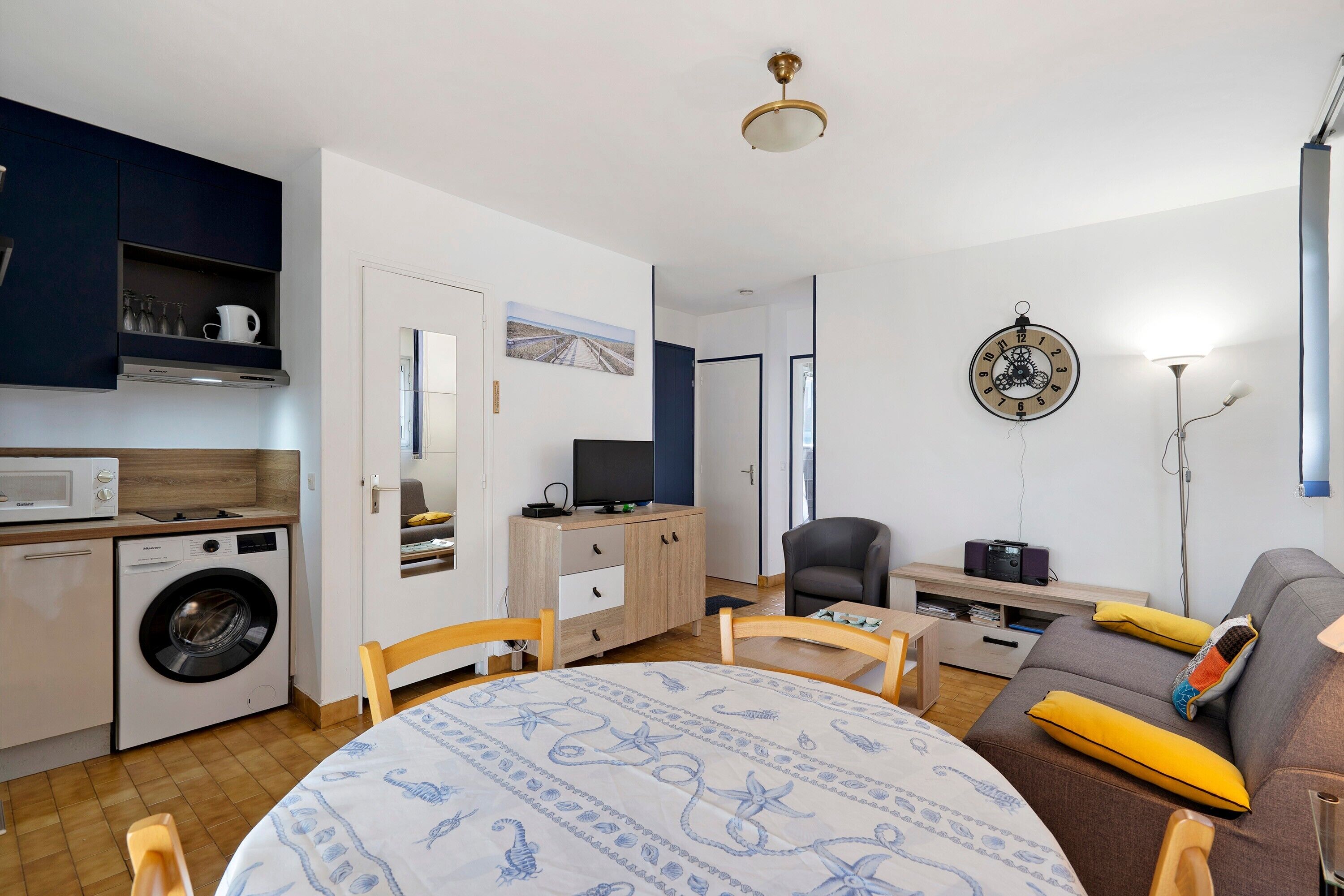 A compact living space with a washing machine, a dining table, a sofa, and a television.