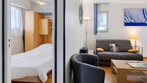 Una habitación con cama, sofá, mesa, lámpara, una bicicleta montada en la pared y un cuadro de veleros.