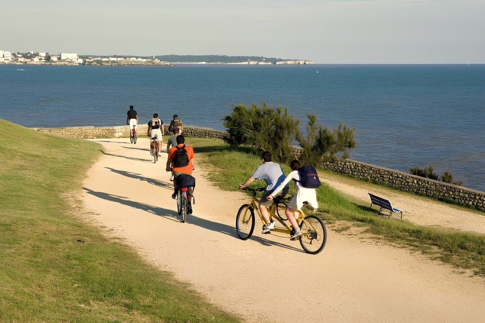 A coastal path with cyclists, a bench, and a view of the sea.