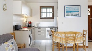 A compact kitchen with a dining area, a washing machine, and a small table with chairs. - Apartment "Les Orphies" with Private Terrace, Shared Garden and Wi-Fi (Vaux-sur-Mer)