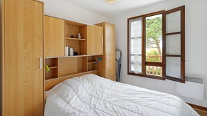 A bedroom with a bed, wooden wardrobe, and a window with a view. - Apartment "Les Orphies" with Private Terrace, Shared Garden and Wi-Fi (Vaux-sur-Mer)